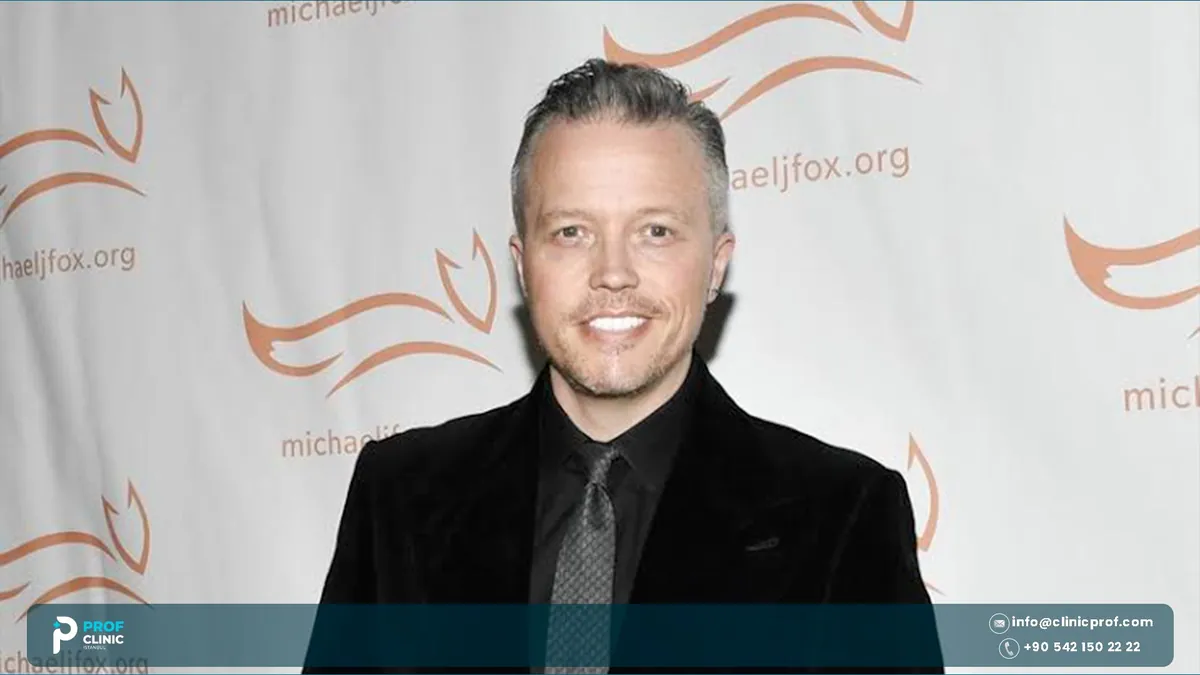Jason Isbell smiling in a black velvet jacket at a charity event backdrop